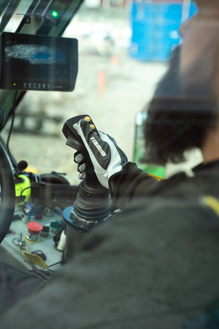 A man uses a joystick to control a construction vehicle wearing gloves.